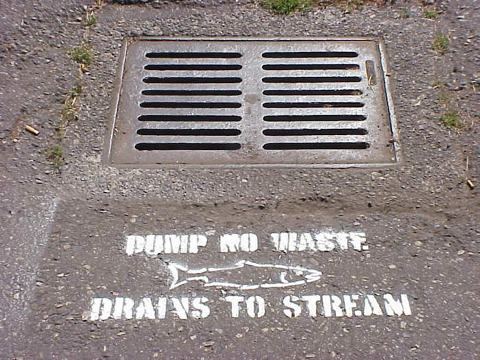 Storm drain on street with stenciled fish and words reading, Dump no waste, drains to stream.